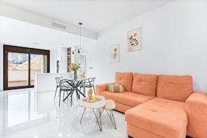 Een moderne woonkamer met een bank, een eettafel met stoelen en kunstwerken aan de muur.