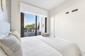 Een slaapkamer met een groot bed, uitzicht naar buiten en een schuifdeur naar een balkon.