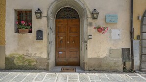 A building entrance with a wooden double door, a welcome mat, a small window with flowers, and a sign above the door. - Room 'Ginepro Double  - First Floor' with Shared Terrace and Wi-Fi (Montecarlo)