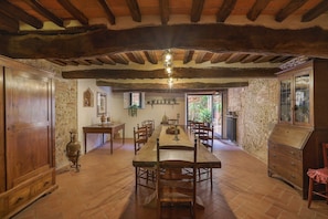 Un espace repas avec une longue table en bois, des chaises et un lustre. Les murs sont en pierre et le plafond est orné de poutres en bois.