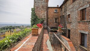 A stone building with a tower, a balcony with potted plants, and a view of the countryside. - Room 'Ginepro Double  - First Floor' with Shared Terrace and Wi-Fi (Montecarlo)