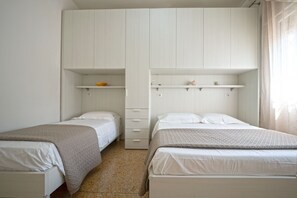 A bedroom with two beds, a wardrobe, and a shelf with a bowl.