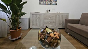Ein Wohnzimmer mit einer großen Kübelpflanze, einer Schale mit getrockneten Blumen, einem Stadtbildgemälde und einem grauen Sofa.