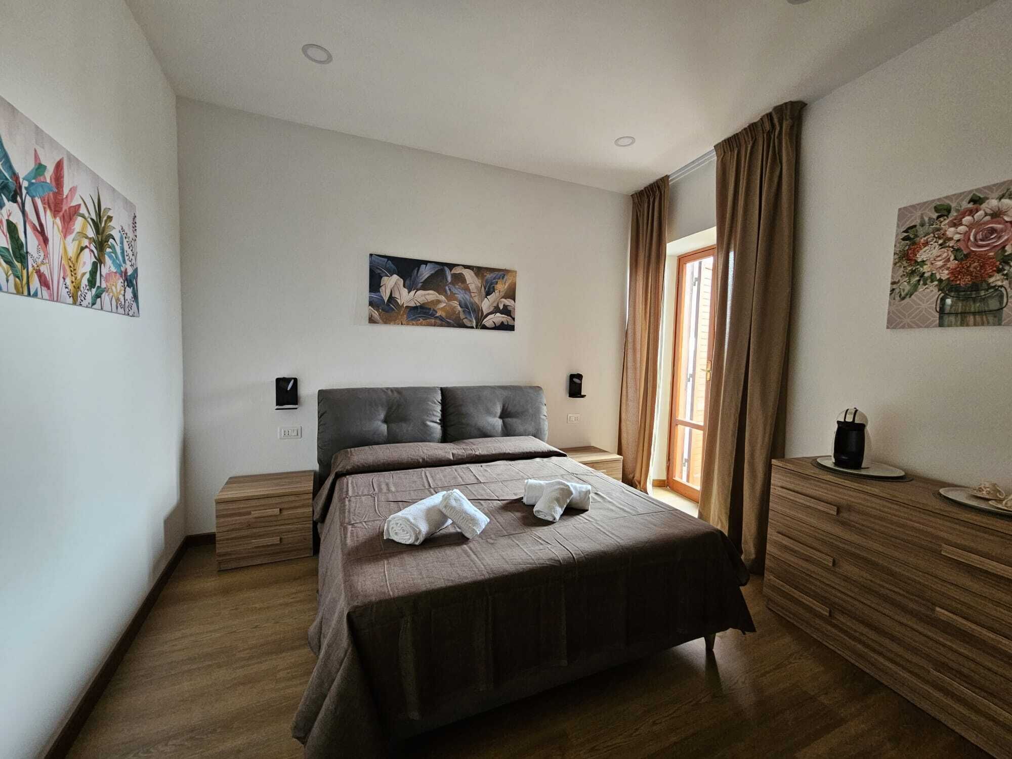 Una camera da letto con un letto grande, pavimento in legno, un quadro al muro e una finestra con tende.
