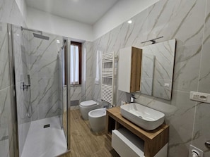 Un bagno moderno con cabina doccia in vetro, un water, un bidet, un lavabo con mobile contenitore in legno e uno specchio.