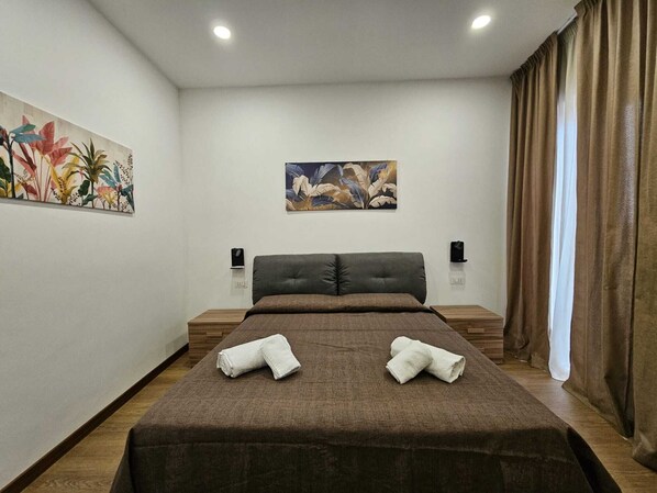 Ein Schlafzimmer mit einem großen Bett, zwei Nachttischen, einem an der Wand montierten Fernseher und einem Bild an der Wand.