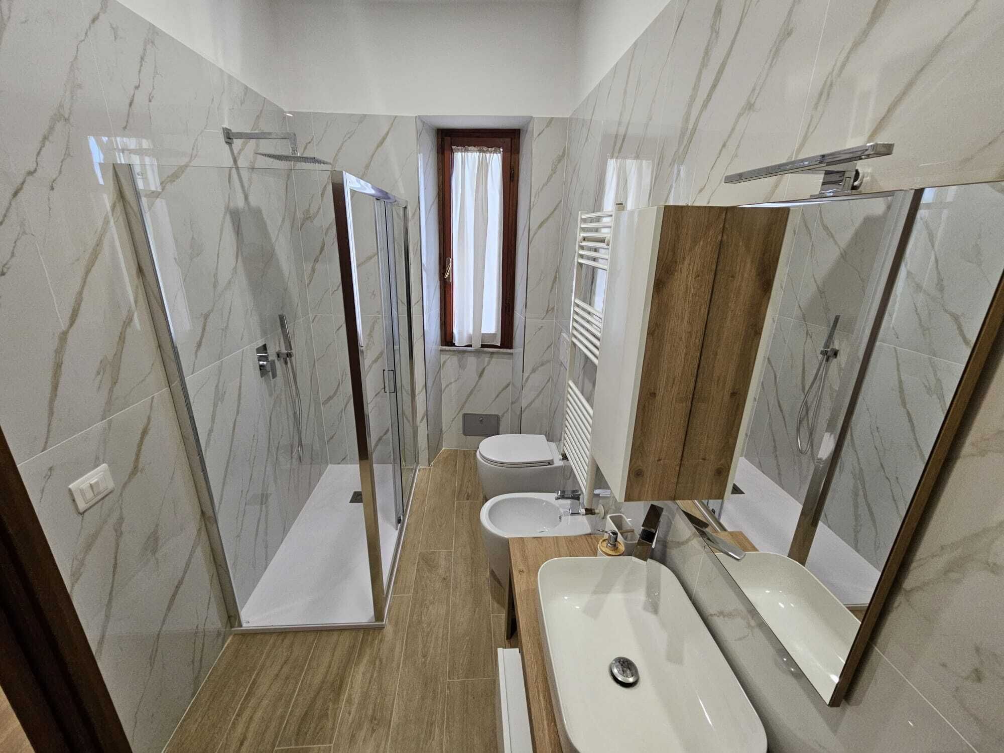 Ein modernes Badezimmer mit einer gläsernen Duschkabine, einem Holzwaschtisch und einem großen Spiegel.