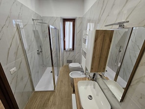 A modern bathroom with a glass-enclosed shower, a wooden vanity, and a large mirror.