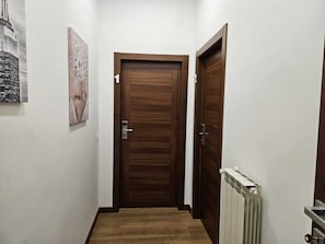 Un corridoio con una porta in legno, un termosifone e un quadro appeso al muro.