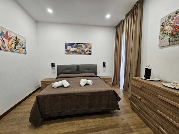Una moderna camera d'albergo con un letto grande, pavimento in legno, una cassettiera in legno e due quadri alle pareti.