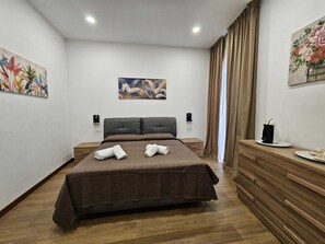 Ein modernes Hotelzimmer mit einem großen Bett, Holzboden, einer Holzkommode und zwei Bildern an der Wand.