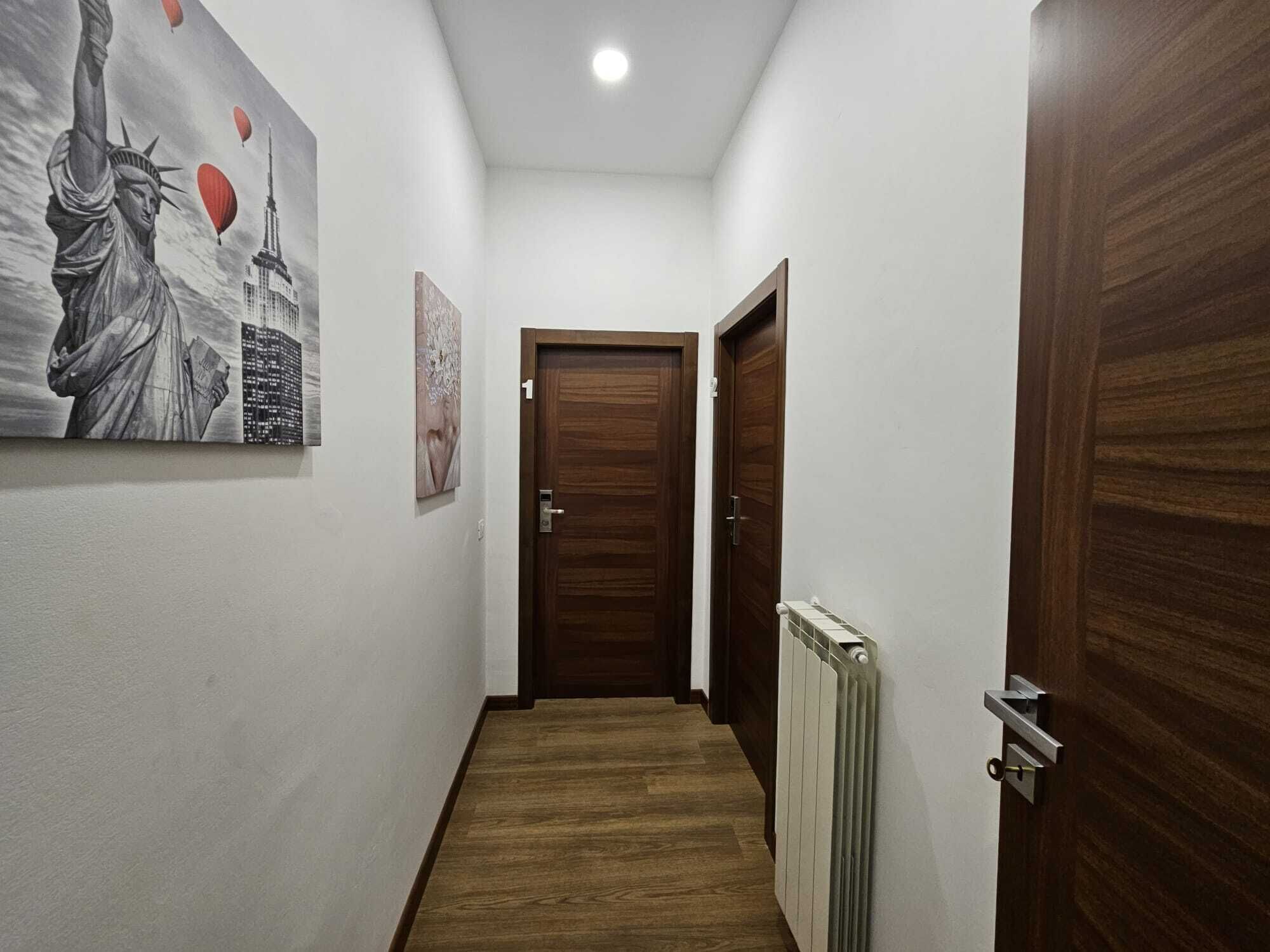 Un corridoio stretto con pavimento in legno, pareti bianche e una porta marrone in fondo.
