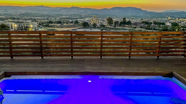 Una terraza de madera con piscina, con vistas a un paisaje urbano y montañas al fondo.