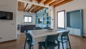 Una cocina moderna con vigas de madera, una zona de comedor con sillas color turquesa y estanterías empotradas.