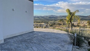Un edificio moderno con un patio empedrado y vistas a un paisaje distante con montañas y una palmera.