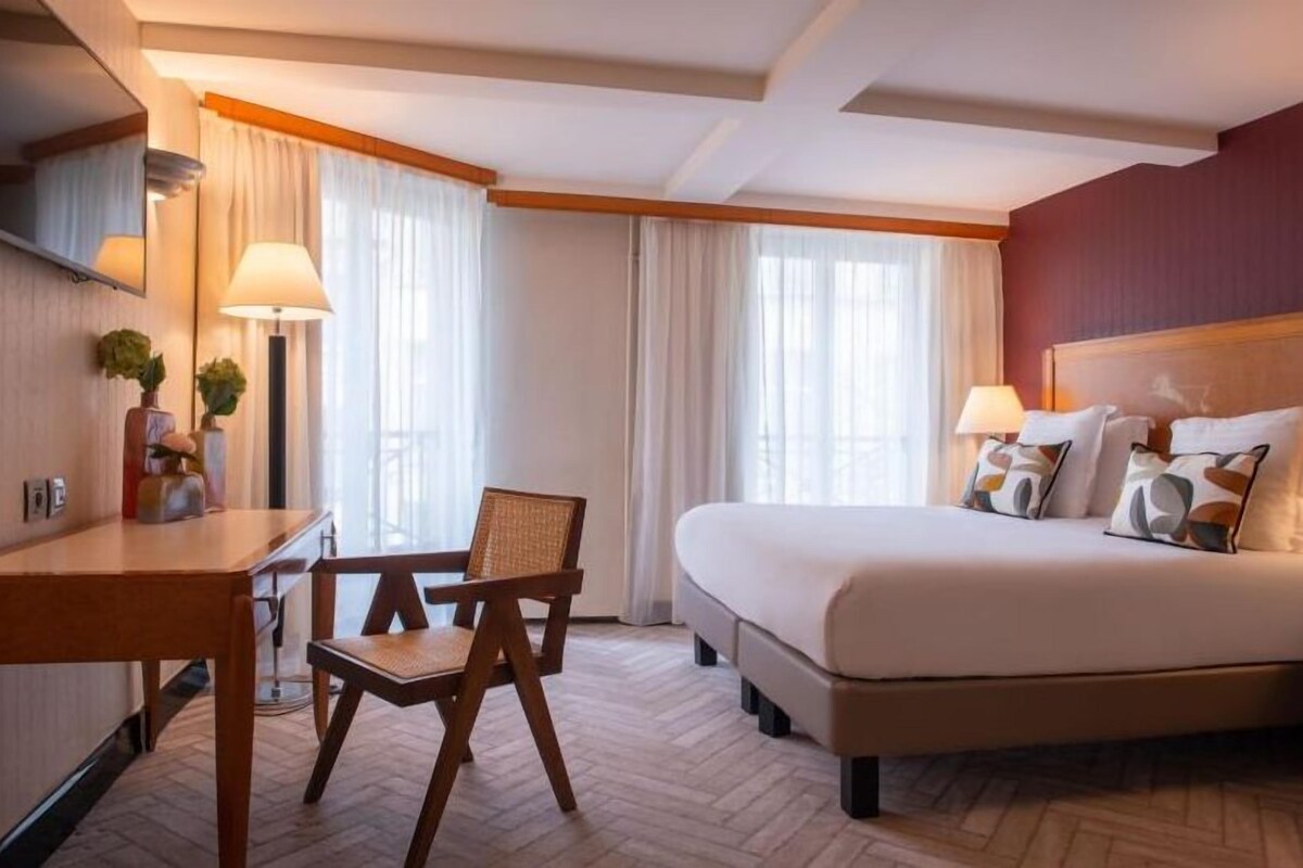 Une chambre d’hôtel avec un lit, un bureau, une chaise et une fenêtre avec des rideaux.