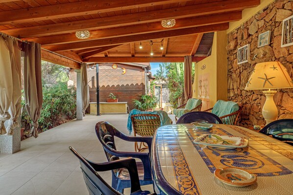 An outdoor dining area with a stone wall, wooden ceiling, and a table with chairs.