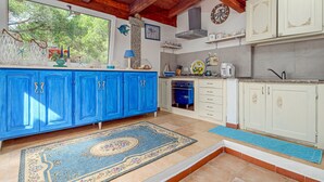 Una cucina con mobili azzurri e bianchi, una colonna in pietra, un orologio e vista su alberi dalla finestra.