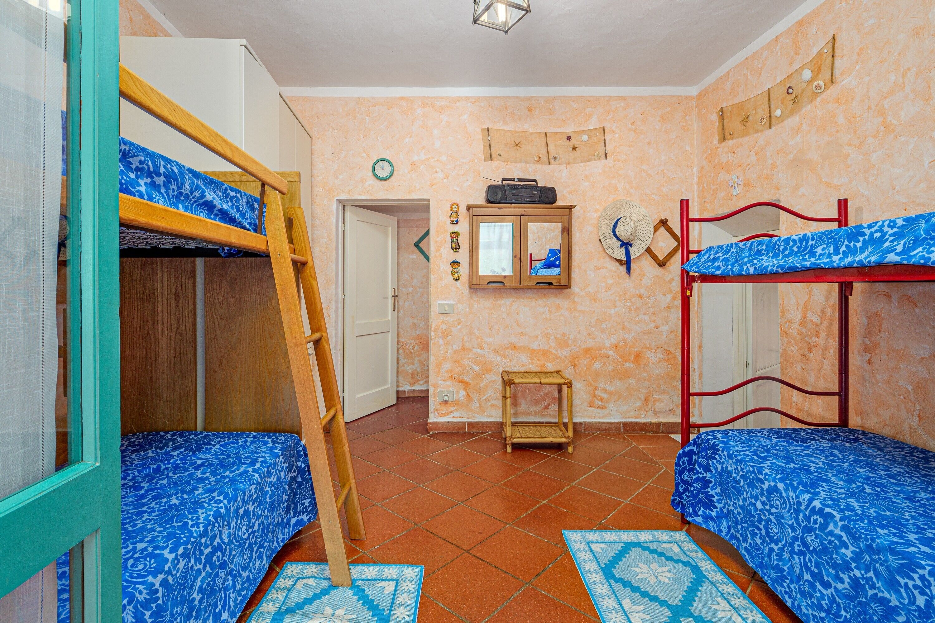 Quarto com beliches, uma escada de madeira, um rádio, um armário pequeno e uma porta.