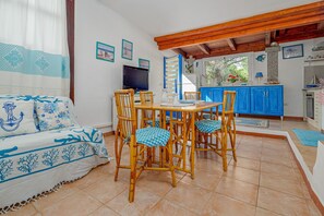 A room with a sofa, dining table with chairs, a TV, and a kitchen area with blue cabinets. - Holiday Home 'Casa Taverna' with Private Terrace (Punta Pietra Bianca)