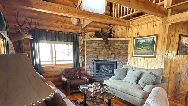 L’intérieur d’une cabane en rondins, avec une cheminée, des meubles en cuir et des têtes d’animaux empaillées accrochées aux murs.