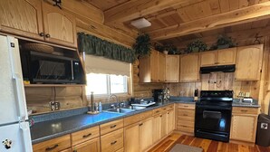 Une cuisine aménagée dans une cabane en bois, comprenant un réfrigérateur, un four à micro-ondes, un évier, une cuisinière et des placards.