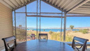 Un patio cubierto con una mesa redonda y dos sillas, con vista a una playa y al agua.