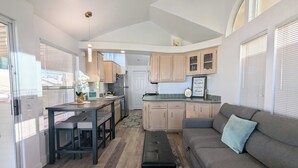 Una cocina compacta con armarios de madera, un comedor con un banco y un sofá gris con un cojín.