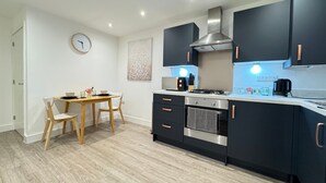 A modern kitchen with dark cabinets, a stainless steel stove, and a dining area with a wooden table and chairs.