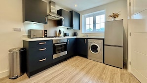 A modern kitchen with dark cabinets, a stainless steel range, a built-in oven, a washing machine, and a refrigerator.