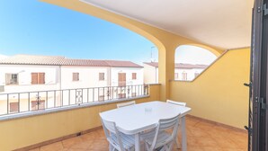 Un balcon avec une table et des chaises blanches, une vue sur des immeubles et un mur jaune.