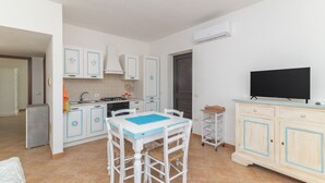 Une cuisine compacte avec des meubles blancs, une table à manger, un téléviseur et un petit réfrigérateur.