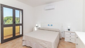 Une chambre à coucher comprenant un lit, une table de chevet, une commode, un appareil de climatisation et une porte-fenêtre coulissante donnant sur un balcon extérieur.