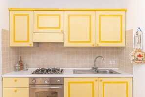 Une cuisine avec des meubles de couleur jaune, une cuisinière à gaz, un évier et un dosseret carrelé.