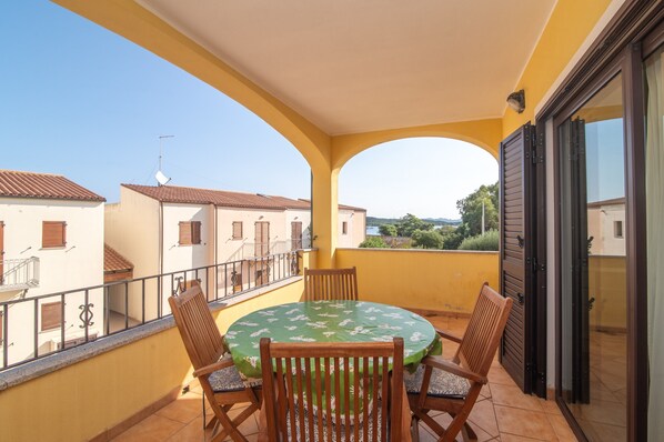 Un balcon avec une table ronde et des chaises, un mur jaune et une vue sur les bâtiments voisins.