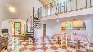 Un vaste espace de vie doté d’un sol à carreaux, d’un escalier en colimaçon, d’une table à manger entourée de chaises et d’une cuisine visible à travers une arche.