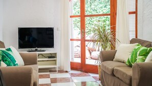 Un salon équipé d’une télévision, de deux canapés, d’une plante en pot et d’une grande fenêtre donnant sur un paysage verdoyant.