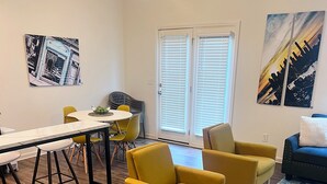 A modern living room with wooden flooring, a dining area with yellow chairs, and a large window with blinds. - New Charming 3-bedroom/2.5 bathroom house in Metro Atlanta area (Decatur)