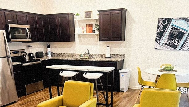 A compact kitchen with dark cabinets, a microwave, and a small dining area with yellow chairs. - New Charming 3-bedroom/2.5 bathroom house in Metro Atlanta area (Decatur)