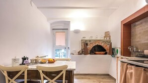 Una cocina con chimenea de piedra, una mesa de comedor con sillas y un ventanal con persianas.