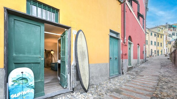 Una estrecha calle adoquinada con edificios a ambos lados, una puerta con una tabla de surf y un letrero con el número 27.