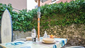 Mesa al aire libre con una tabla de surf, una botella de vino, copas y fruta.