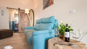 Una habitación acogedora con un sofá azul, una mesa de centro de madera con copas de vino y una botella, y una planta en maceta.