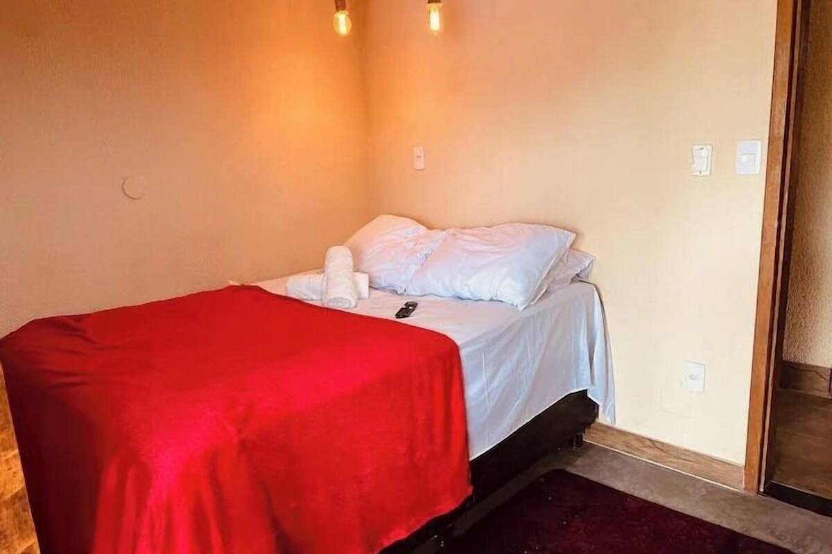 A single bed with a red bedspread, white pillows, and a remote control on the bed.