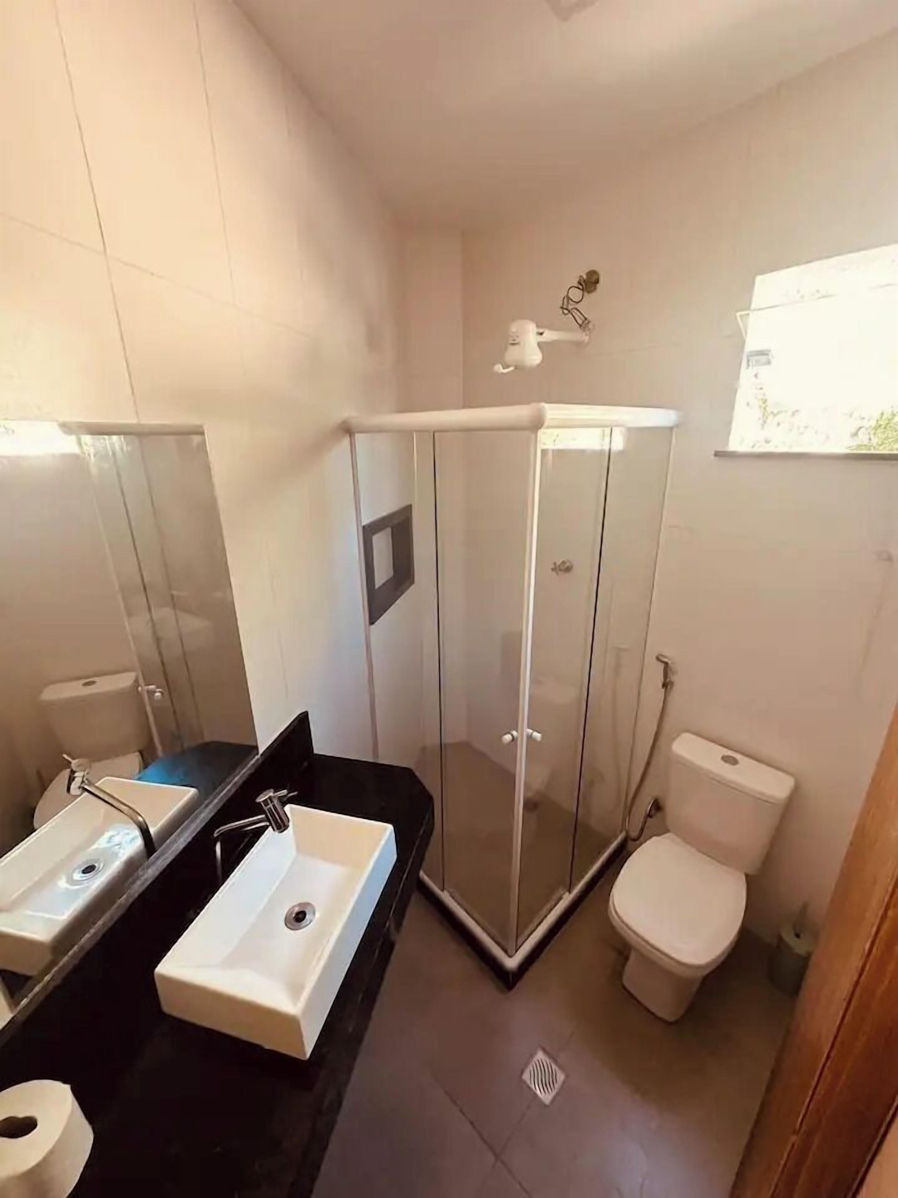 Un baño con cabina de ducha de vidrio, inodoro y dos lavamanos con espejos.