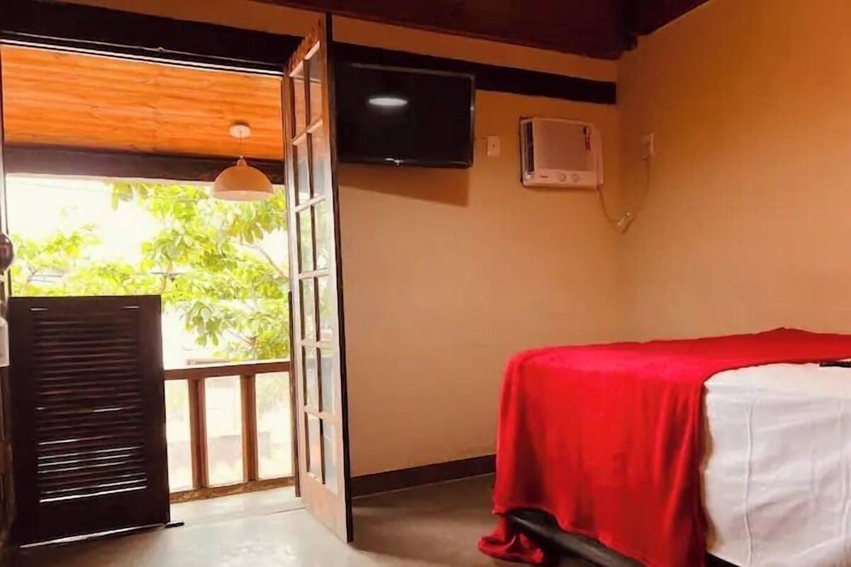 A room with a bed, a television, and a window with a view of greenery.