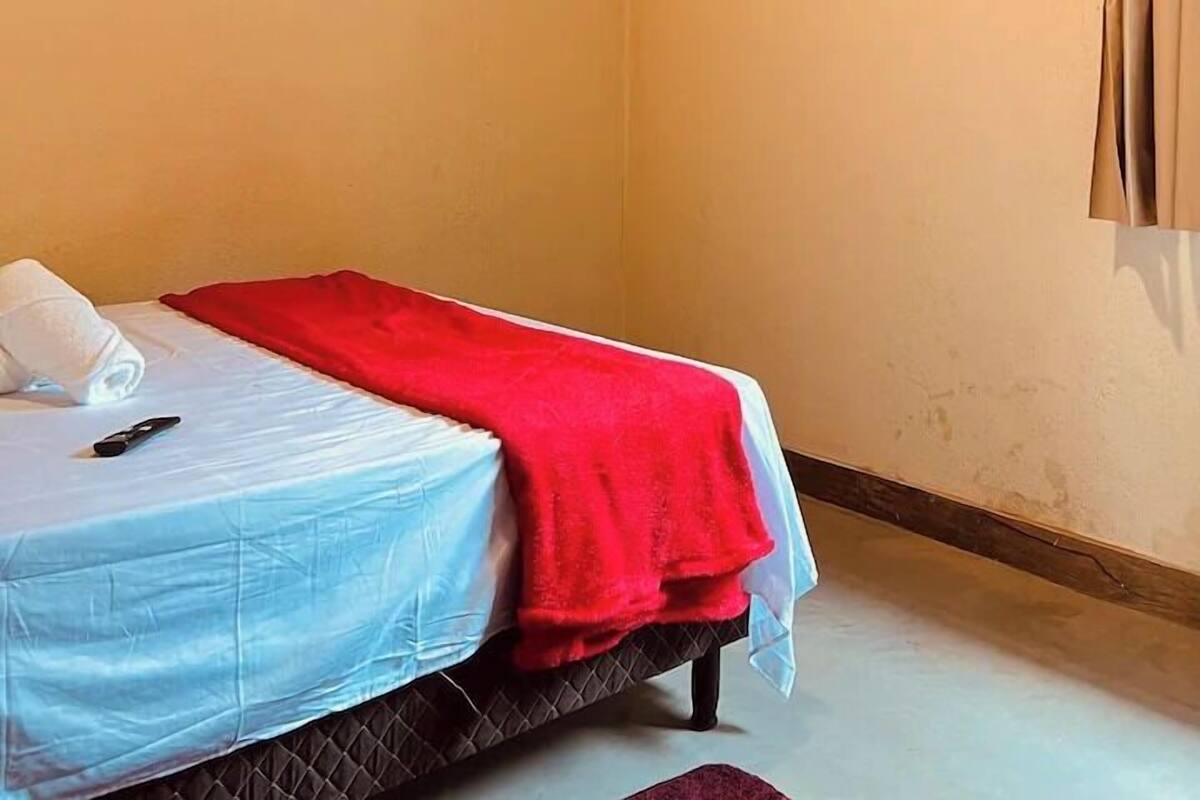 A single bed with a red blanket, a television mounted on the wall, and an air conditioning unit.