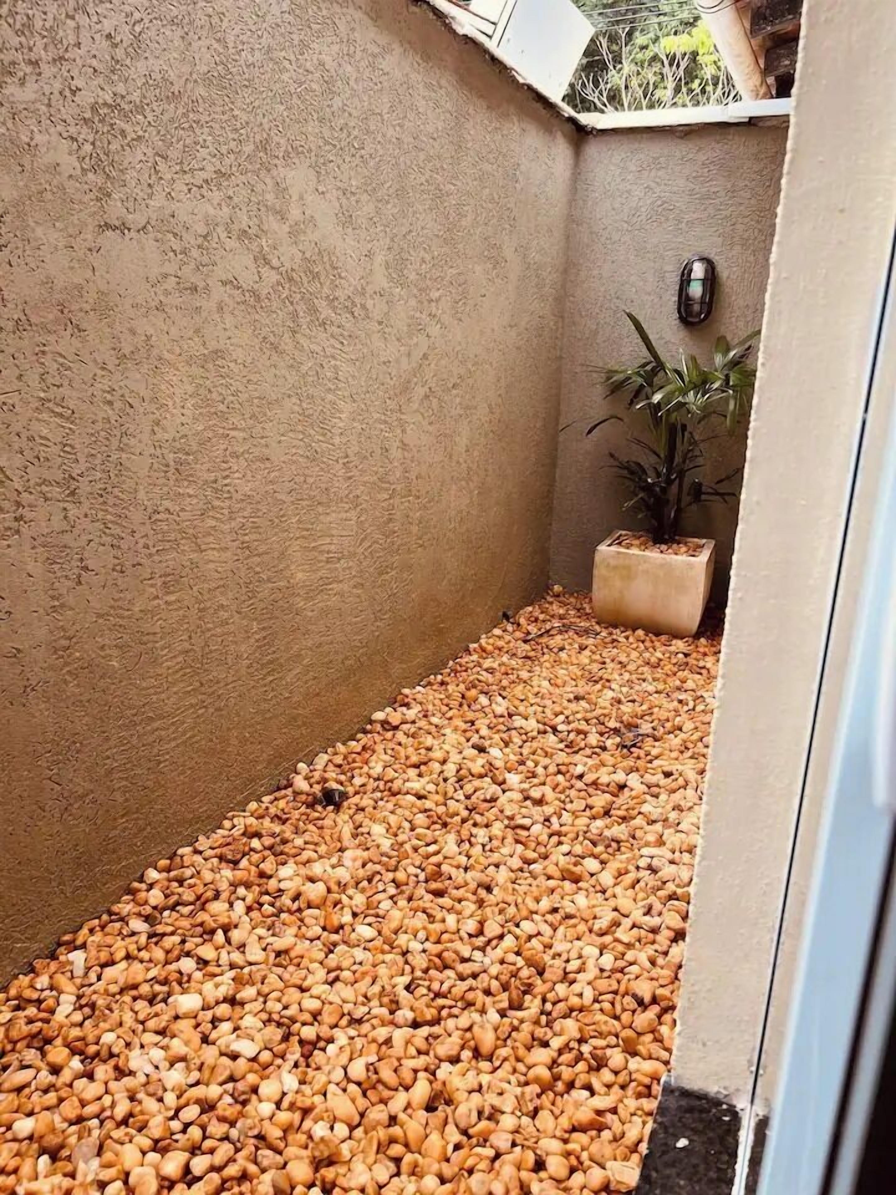 A small, enclosed space with a textured beige wall, a floor covered with small pebbles, a potted plant, and a small decorative item on the wall.