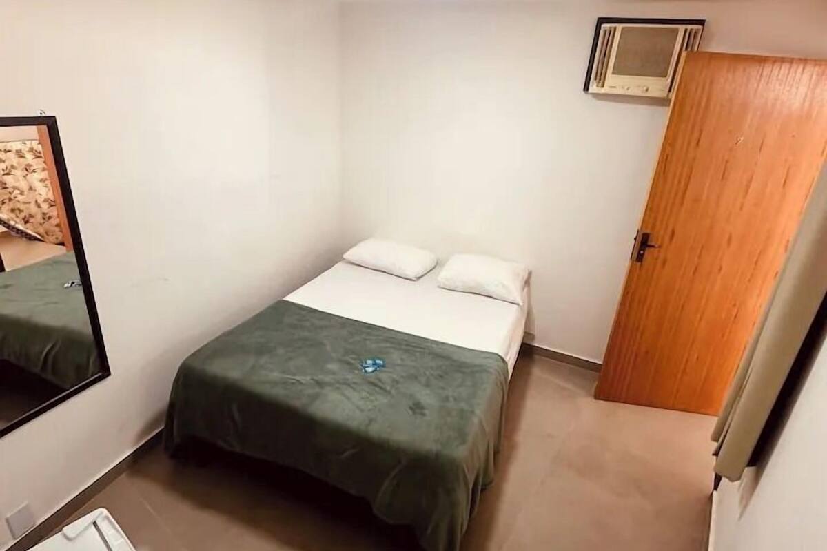 A small, clean room with a bed, a mirror, a heater, and a door.