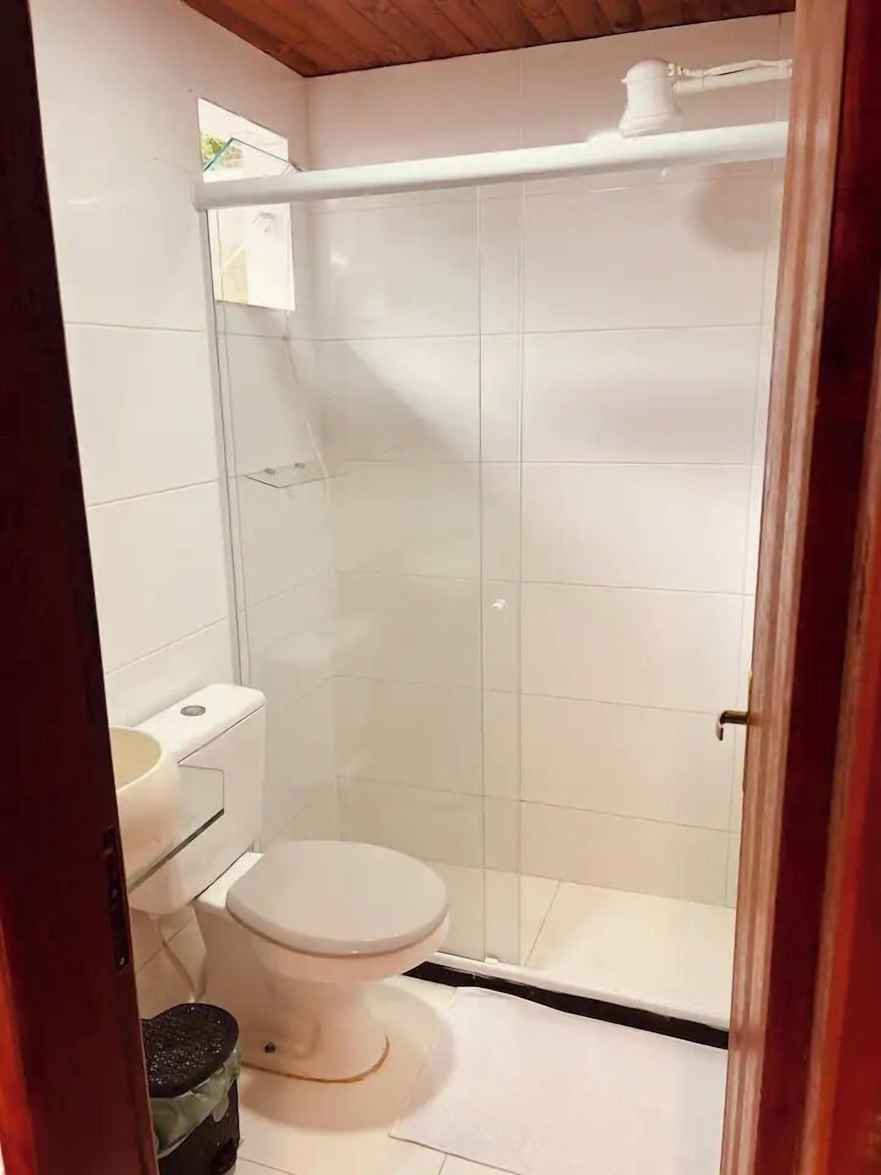 Une petite cabine de douche fermée, dotée d’une porte en verre, de toilettes blanches et d’une petite poubelle.